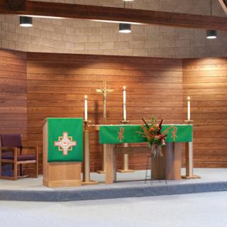 A serene view of a church altar, featuring candles and a green cloth, set against a backdrop of warm wooden walls.