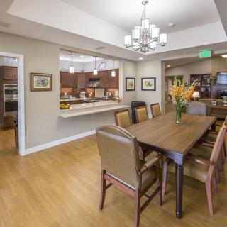 A modern dining room with a wooden table and chairs, featuring an open view to the kitchen area.