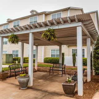 An outdoor pergola with benches and hanging plants situated in front of a residential building.
