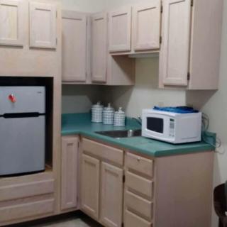 A compact kitchen with beige cabinets, a microwave on the countertop, and a small refrigerator.