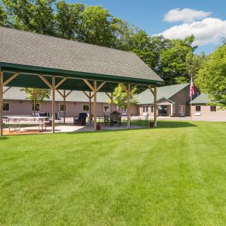 A sunny day with a pavilion and surrounding lawn, backed by trees.