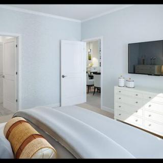 A modern, minimalist bedroom with light-colored walls, featuring a bed, a dresser, and a wall-mounted TV.