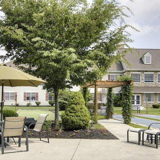 A well-maintained garden patio with furniture, surrounded by lush greenery and adjacent to a residential building.