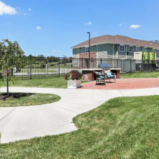 A sunny outdoor recreational area with a tennis court, walkway, and benches near a building.