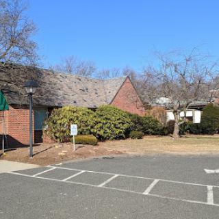 A serene view of a brick building in a parking area, surrounded by trees under a clear blue sky.