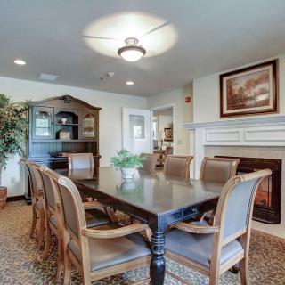 A cozy dining room with a large table, surrounded by chairs and adorned with a chandelier, fireplace, and decorative elements.