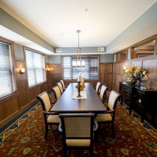 Elegant dining room with a long table, surrounded by chairs and enhanced by wood paneling and decorative lighting.