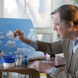 An artist in their studio working on a sky-themed painting.