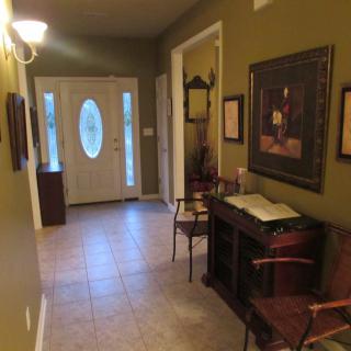 A warmly lit hallway with a tiled floor, featuring an ornate front door, decorative furniture, and framed artwork on the walls.