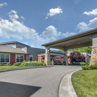 A modern building with a covered driveway and landscaped surroundings under a partly cloudy sky.
