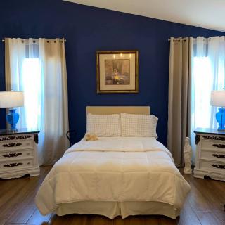 A cozy bedroom with a white bed against a blue accent wall, flanked by nightstands and matching lamps.