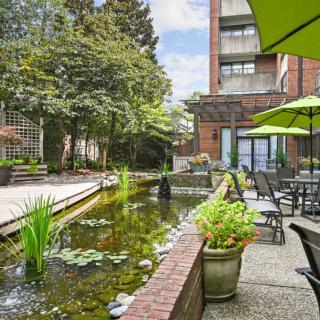 A tranquil outdoor garden with a pond and seating area under green umbrellas, adjacent to a building.