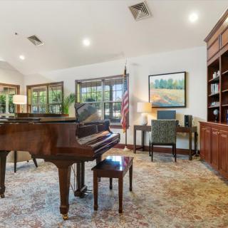 A cozy living room with a grand piano and office area featuring a bookshelf, desk, and artwork.