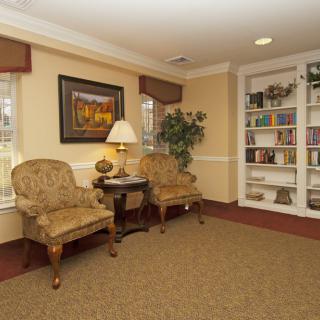 A cozy living room with two upholstered chairs, a side table with a lamp, and a bookshelf filled with books.