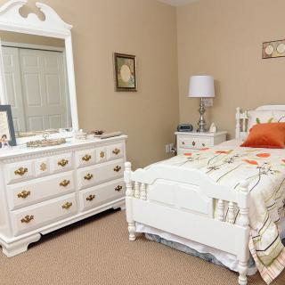 A cozy bedroom with white furniture, including a bed and a dresser with a mirror.
