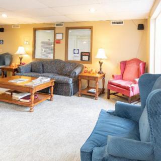 A cozy living room with sofas, armchairs, and a coffee table, warmly lit by lamps.