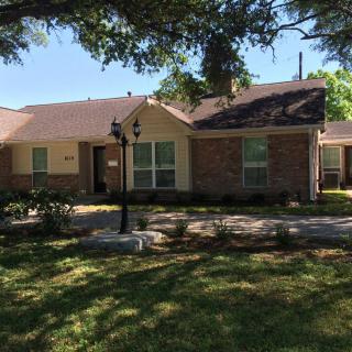 A suburban brick house with a well-kept front yard and large trees providing shade.
