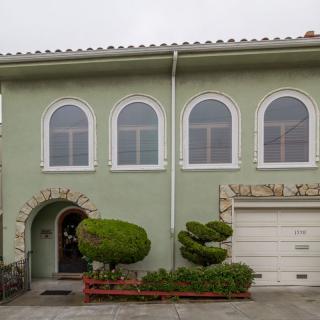A two-story house with arched windows and a green exterior, featuring a garage and well-maintained landscaping.