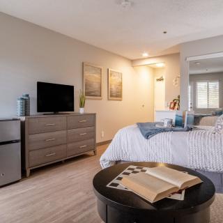 A cozy, modern bedroom with a bed, dresser, and television, featuring warm lighting and an open book on the table.