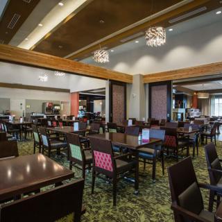 A modern restaurant interior with empty tables and chairs, featuring stylish lighting and a carpeted floor.
