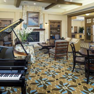 A spacious living room featuring a grand piano, elegant furniture, and a patterned carpet.
