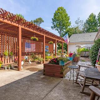 A sunny patio with a pergola, colorful plants, and outdoor seating area.