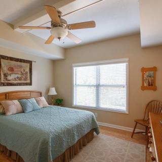 A cozy bedroom featuring a bed with blue bedding, a ceiling fan, and natural light from the window.