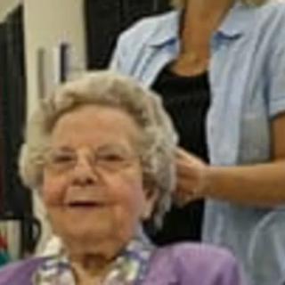 An elderly woman smiling while getting her hair styled indoors.