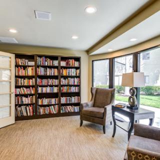 A cozy reading nook featuring a bookshelf filled with books, comfortable chairs, and ample natural light.