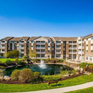 A modern apartment complex featuring landscaped gardens and a central pond with a fountain.