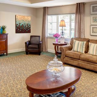 A cozy living room with a sofa, armchair, and wooden coffee table, featuring elegant decor and a large window.