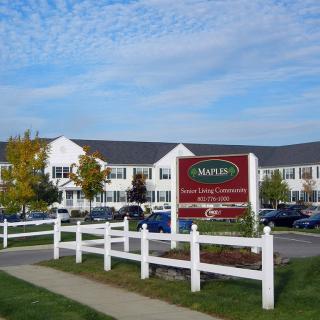 A large building with a sign in front, surrounded by a parking lot and white fence on a clear day.