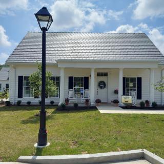 A white house with a solar roof and a well-maintained front yard, featuring a lamp post and a covered porch on a sunny day.
