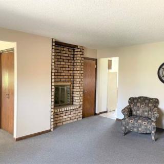 A living room with a brick fireplace, carpeted floor, and a patterned armchair near a wall clock.