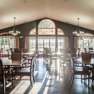 A spacious dining room with large arched windows allowing natural light to flood the space, featuring neatly arranged tables and chairs under elegant chandeliers.