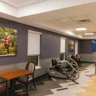 A room with exercise equipment, tables, chairs, and artwork on the walls.