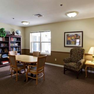 A cozy library room with a table, chairs, and a bookshelf near a window.