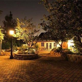 A serene garden illuminated by soft lights at night, featuring a cozy house in the background.