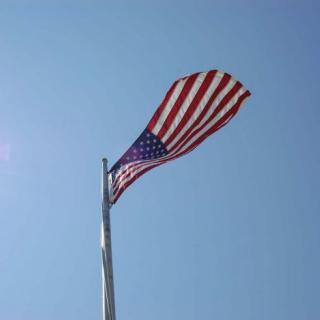 An American flag waving on a flagpole against a clear blue sky.