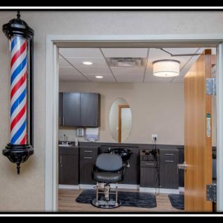 Interior view of a barbershop featuring a barber pole, chair, and mirror.