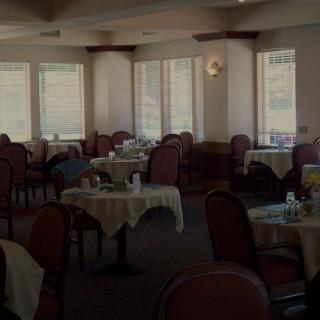 An empty dining area with neatly arranged tables and chairs, illuminated by natural light from the windows.
