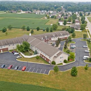 Aerial view of a building complex with a parking lot, surrounded by fields and residential areas.