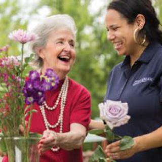 An elderly woman and a young woman enjoying a moment together in a garden with flowers.