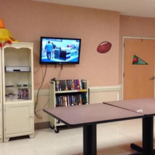A cozy community center TV room with books, a mounted television, and tables for activities.