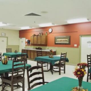 A dining room with neatly arranged tables and chairs, featuring a small kitchen area in the background.