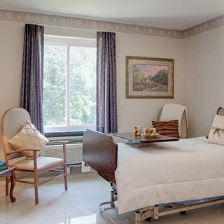 A serene hospital room featuring a bed, comfortable chair, and natural light streaming through the window.