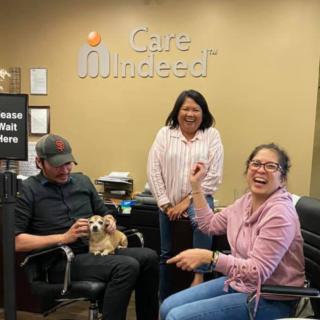 Three people in an office enjoying their time with a small dog.