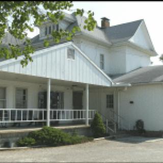 A white residential house with a porch and surrounding trees.