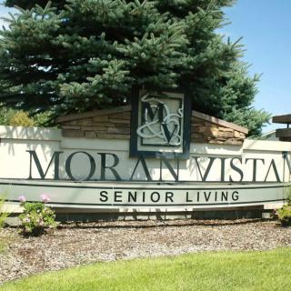 Entrance sign for Moran Vista Senior Living surrounded by greenery and trees.