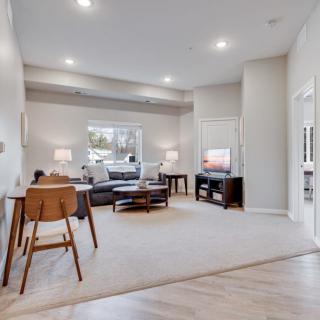 A modern and spacious living room featuring neutral colors, a comfortable sofa, wooden flooring, and a television.